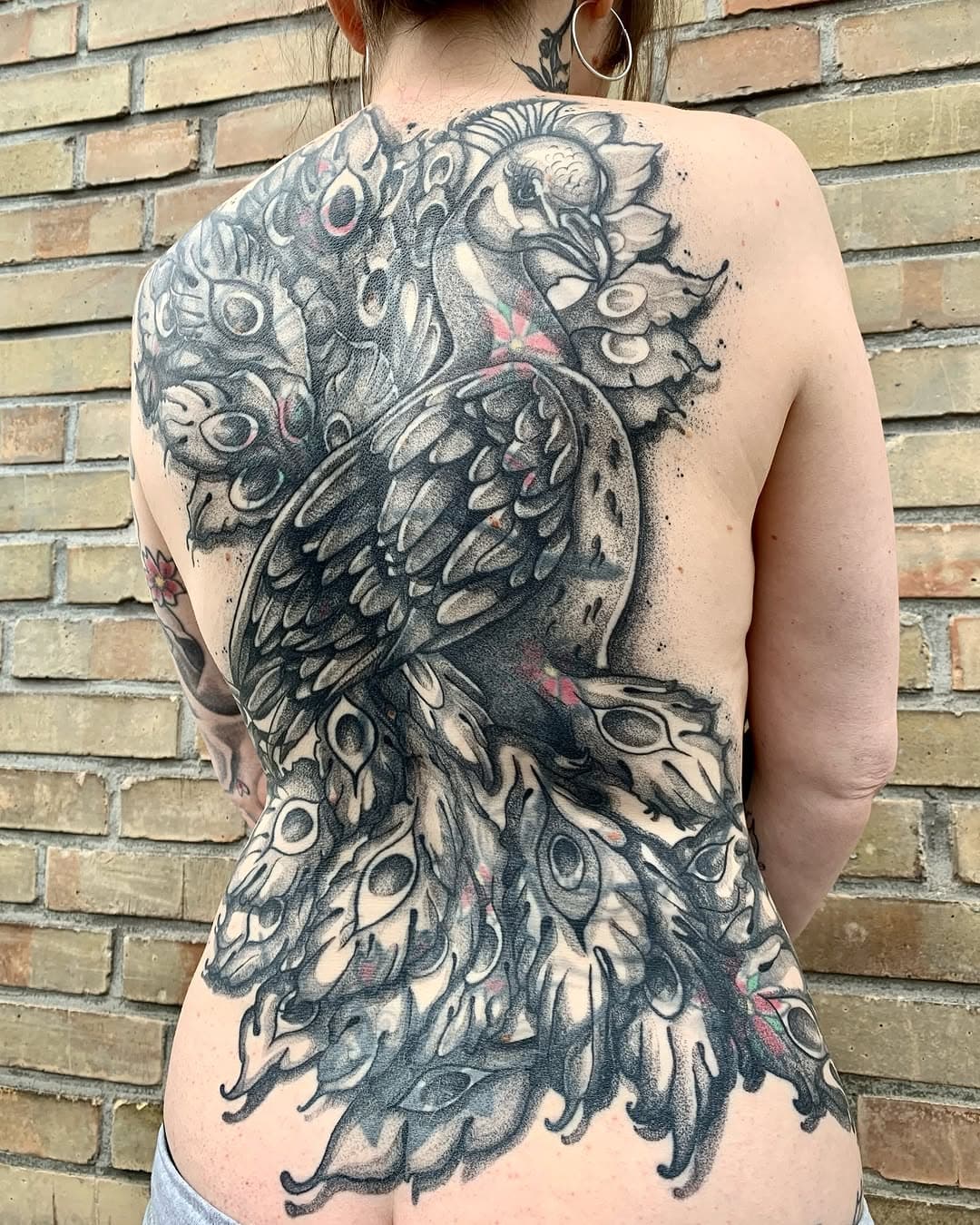 WE DID IT!!! • LOVE LETTER TO MY CLIENT
Liebste Karen,
im März 2024 hast du mir gesagt, dass du dein mehr als 20 Jahre altes Rückentattoo covern lassen möchtest. Deine einzige Vorgabe an mich war, dass es ein Pfau werden soll, für alles weitere hast du mir einfach mal komplett freie Hand gelassen…
Mein Hirn ist natürlich sofort angesprungen (ja, das passiert tatsächlich dann und wann 😁), und ich habe dir am selben Abend gleich noch eine erste grobe Skizze mit meinen Visionen geschickt. Du warst sofort genau so begeistert wie ich, und dann haben wir Termine gemacht.
Im Juli 2024 ging es dann los, in der ersten Session habe ich sechs Stunden lang kreuz und quer Linien, Linien und nochmals Linien über deinen ganzen Rücken gezogen. Und du hast wie ein wahrer Champ so toll mitgemacht, kein einziges Mal gejammert oder gezuckt. 
In allen weiteren Sessions – und das waren einige – haben wir uns gemeinsam durch viele Federn, Schatten, Dots und Dotties geschnattert und gelacht, und jedes Mal war es einfach nur die reine Freude, an und mit dir zu arbeiten.
Und nun ist das Werk vollbracht. Unser Pfau ist fertig. Und ich bin dir von ganzem Herzen unendlich dankbar für dein Vertrauen, für deine Tapferkeit, für die Gespräche mit dir und vor allem dafür, dass es dich gibt. Du bist großartig, und ich hab dich unfassbar lieb ♥️
