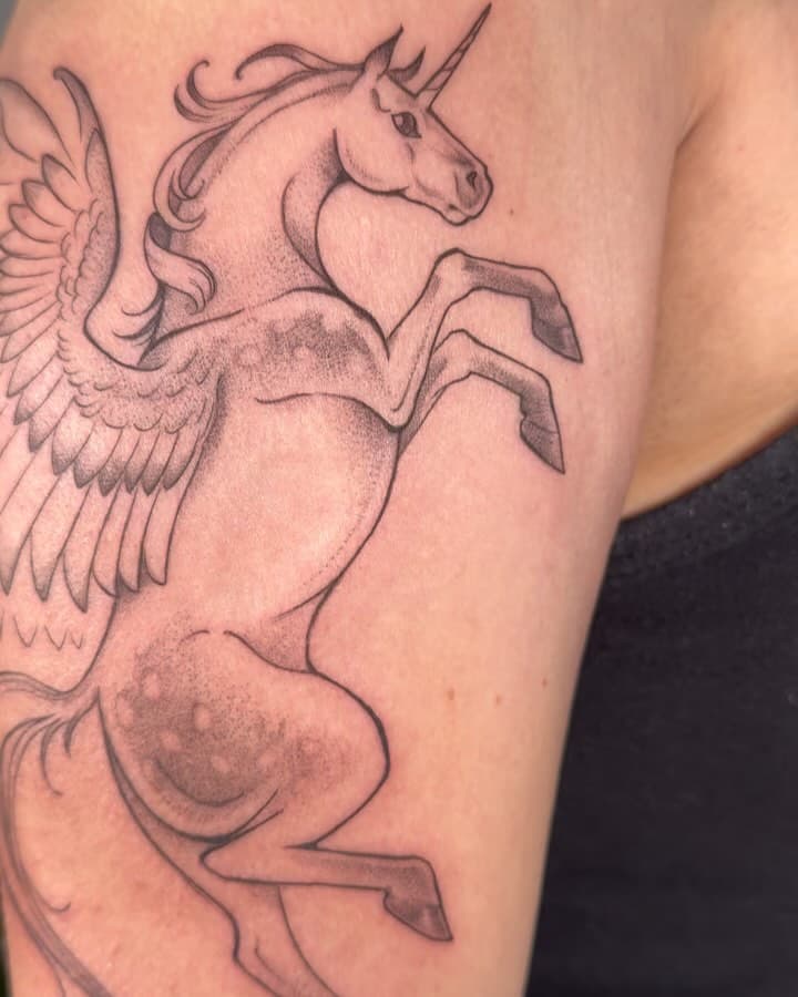 Pegasus Unicorn for Ana from a few weeks ago! Thank you Ana for going bigger than we anticipated, I’m happy with the details✨

Posting feels strange lately and I have a huge backlog. I’m still over here though, still tattooing. I hope yall are making sure to look after yourselves, whatever that means for you 💛

.•.•.•.•.•.•.•.•.•.•.•.

Accessible Description:

All slides document a black and gray tattoo of a dapple gray unicorn Pegasus leaping upward on Ana’s outer upper arm, wings beginning to unfurl. The wings wrap around the back of Ana’s arm with particularly long, curving primary feathers